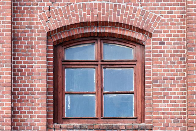 Arched wooden window in a red brick wall, representing CNC-machined window components like sash, sill, and jambs.