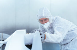 A technician in protective gear inspecting and painting a fiberglass part, highlighting C.R. Onsrud CNC machines' precision in boatbuilding applications.